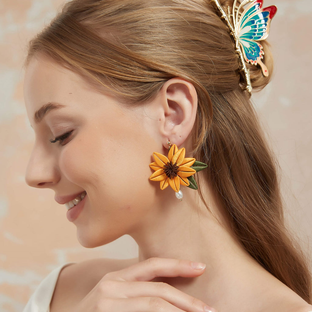 Brighten up your look with our Marigold Sunflower Drop Earrings, a perfect blend of nature-inspired beauty and artisanal craftsmanship. Each earring features a stunning sunflower, delicately accented with two uniquely shaped green leaves, creating a vibrant and organic feel. Twined with intricately colored thread weaving, these earrings offer a unique, handcrafted touch. Designed to be lightweight and comfortable, they’re perfect for everyday wear or adding a cheerful statement to any outfit.