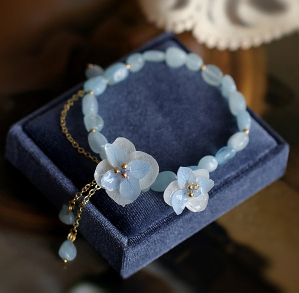  Introducing our exquisite Blue Hydrangea Crystal Beaded Bracelets, where the timeless beauty of hydrangea blossoms meets the captivating allure of blue beryl crystals. Each bracelet is meticulously handcrafted with care, featuring stunning blue beryl crystals that shimmer with every movement, capturing the essence of tranquil waters and endless skies. Adorned with intricately crafted blue hydrangea charms, these bracelets exude a delicate floral elegance that adds a touch of nature-inspired charm to any ensemble